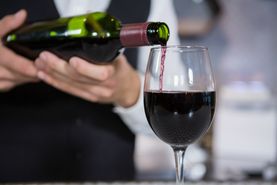 Mid section of bartender pouring red wine on glass in bar counter